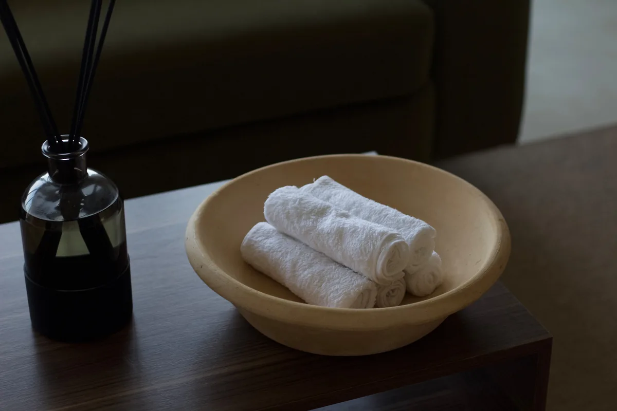 Rolled white towels in a stone bowl beside a reed diffuser in the studio lounge